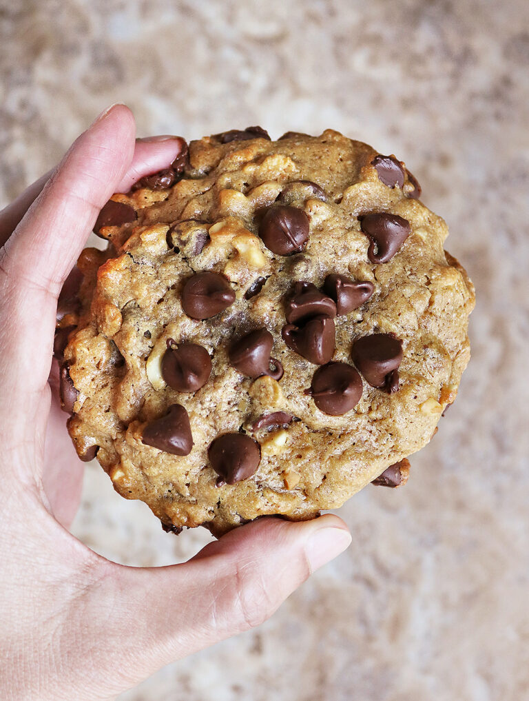 Close-up of a flourless collagen peanut butter chocolate cookie with melting chocolate chips in a hand