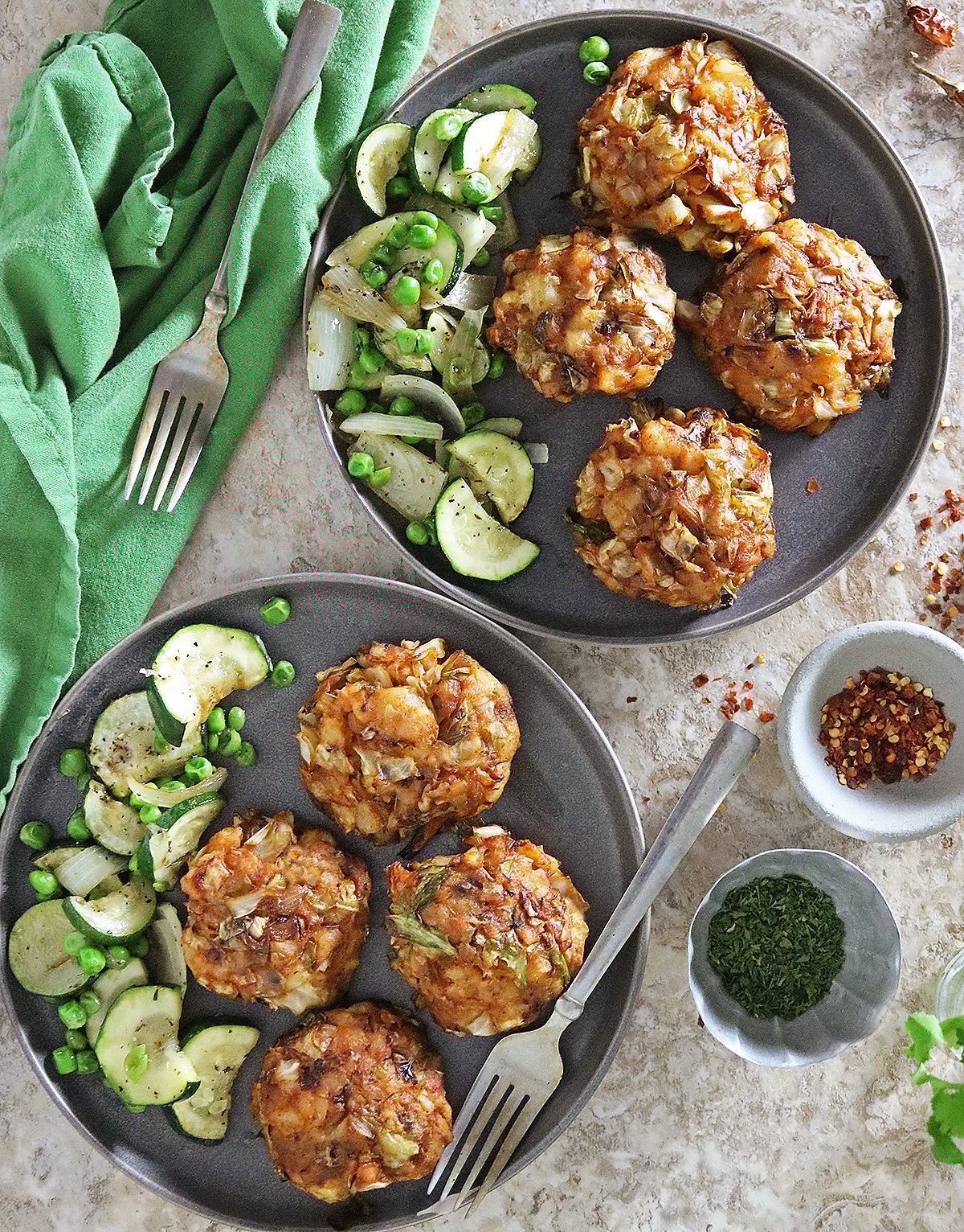 Two plates with Delicious spiced cabbage cakes with some sautéed cucumbers on gray plates with a green napkin.