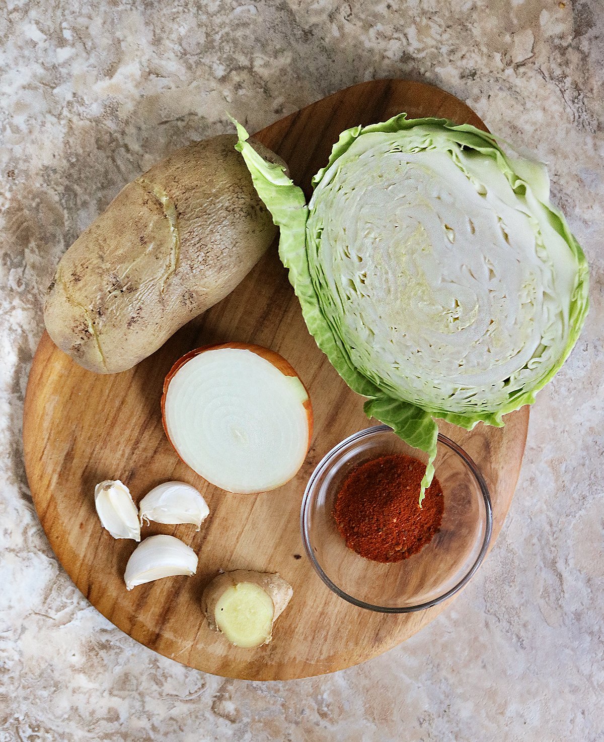 The Ingredients to make Cabbage cakes sitting on a wooden oval board on a brown marble bakground.