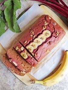 Easy Delicious beet banana bread on a parchment lined board with a banana and beet next to it.