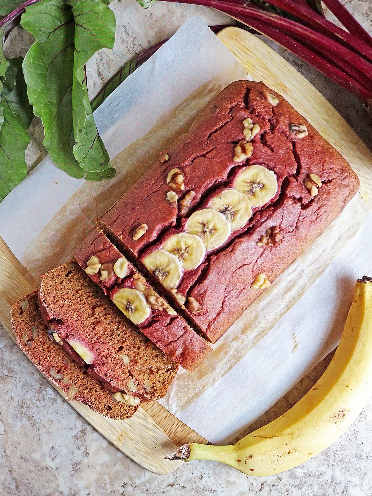 Easy Delicious beet banana bread on a parchment lined board with a banana and beet next to it.