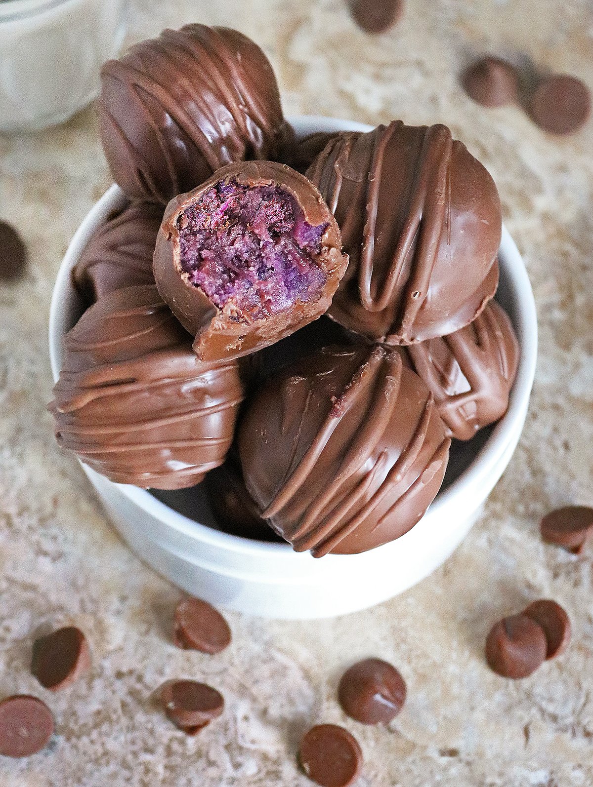 The Best 3 ingredient truffles with purple sweet potato sitting in a bowl. One has a bite taken out of it so the purple inside shines through.