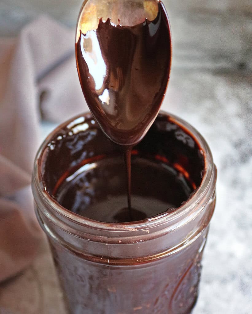 Easy Sugar-free chocolate syrup dripping from a spoon into a jar.