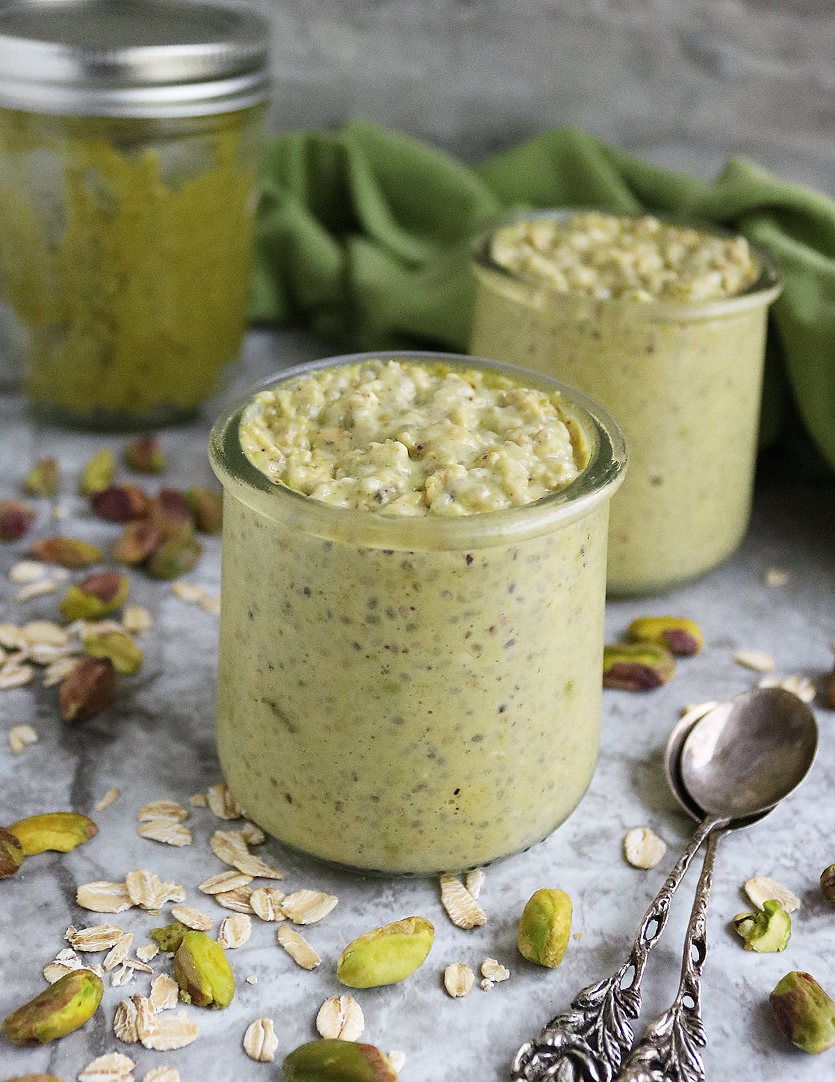 Easy delicious pistachio overnight oats with a jar of homemade pistachio butter in the background, all on a gray marble background.