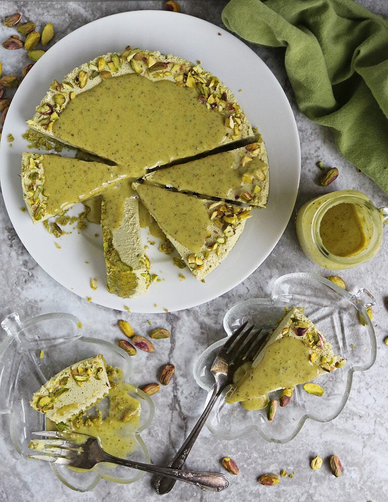Messy and delicious Pistachio keto no bake cheesecake on a white plate with a few slices on small glass serving plates.