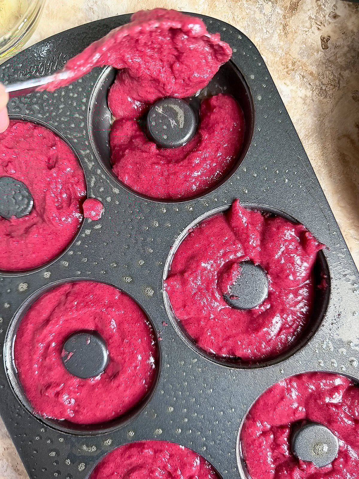 Spooning the naturally colored, vibrant pink batter into a donut pan