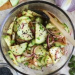 Totally addicting Harissa Cucumber Onion Salad in a large glass bowl with sesame seeds on the side.