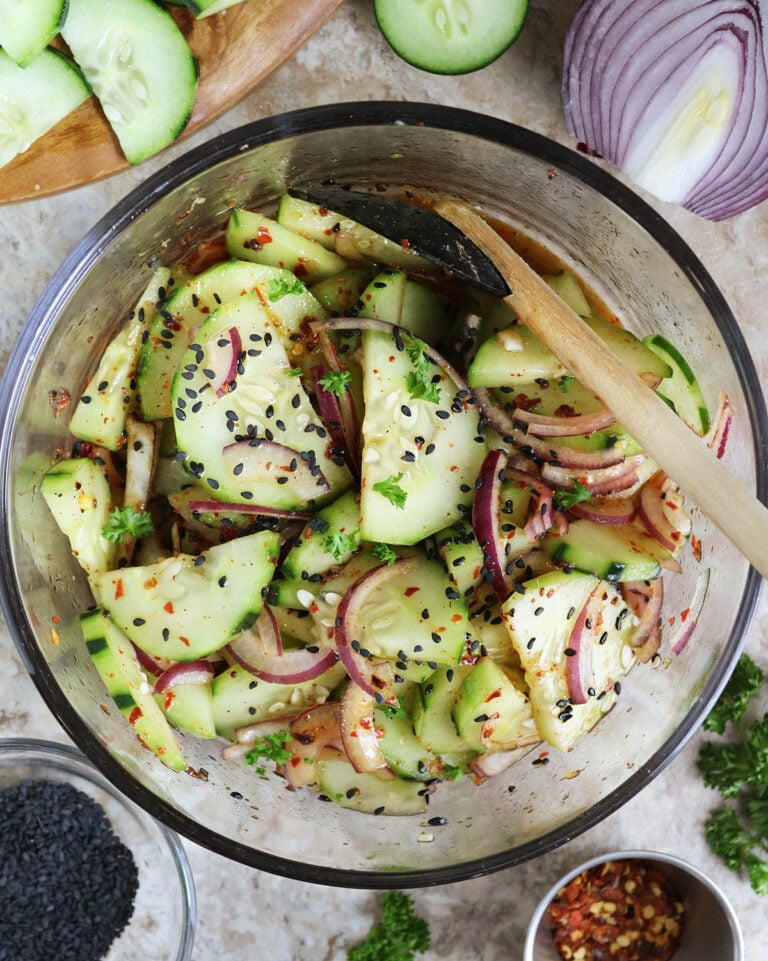 Totally addicting Harissa Cucumber Onion Salad in a large glass bowl with sesame seeds on the side.