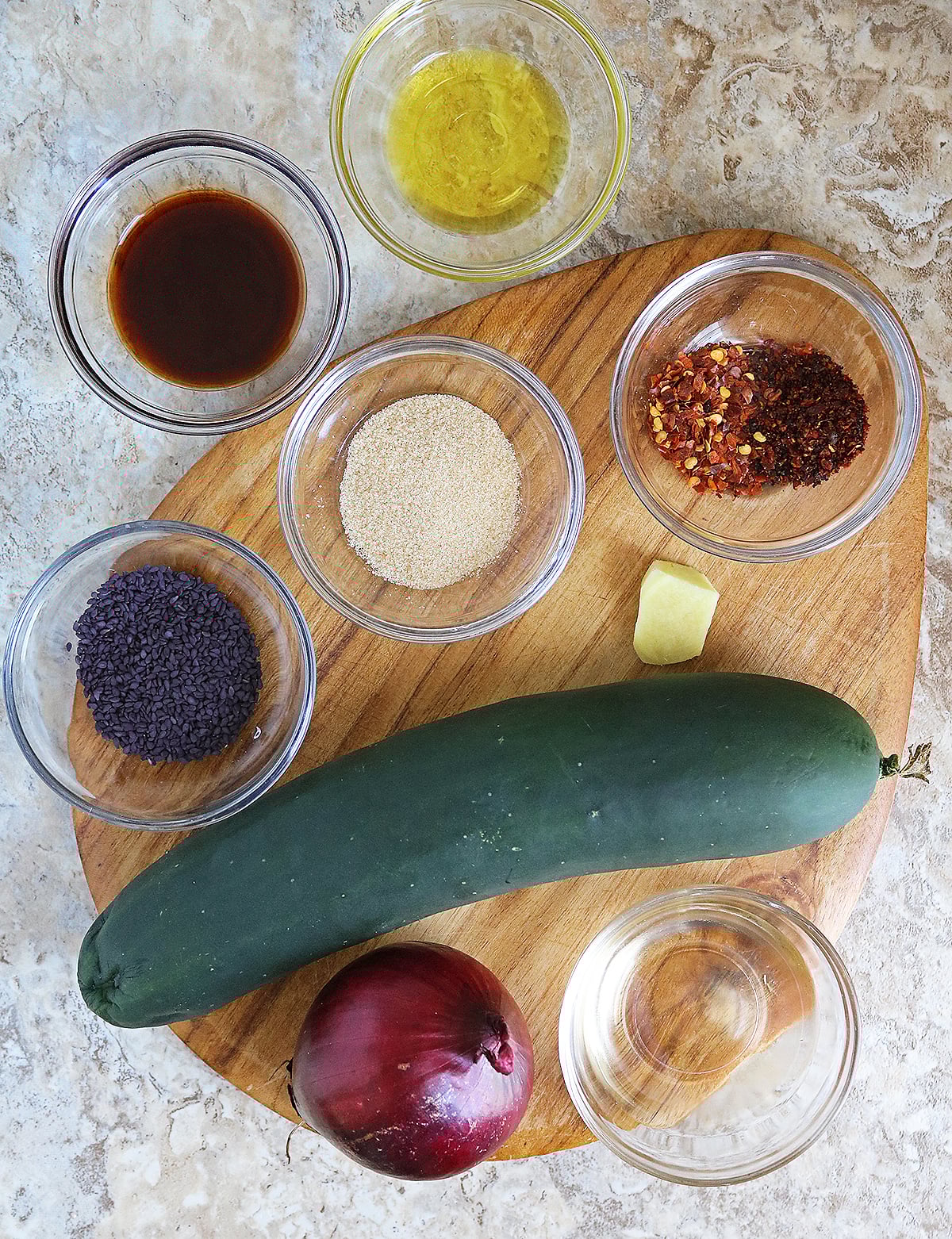 9 ingredients to make a delicious fusion spin on cucumber salad on a gray marble board.