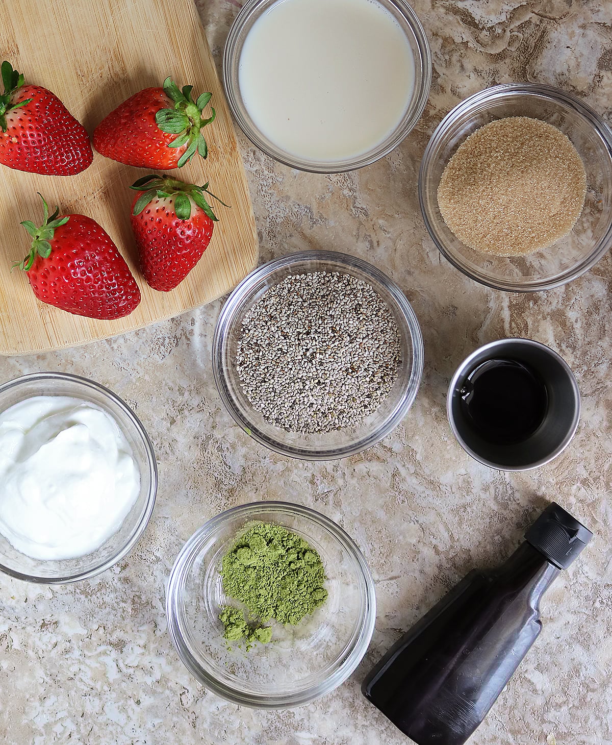 8 ingredients to make matcha chia pudding with yogurt on a brown marble background.