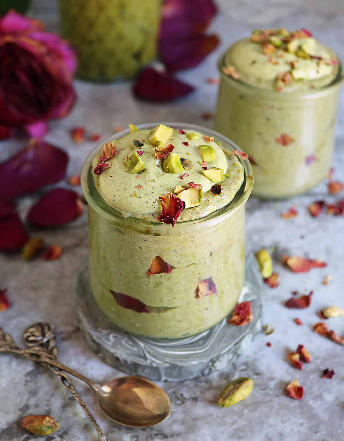 Quick and easy pistachio rose chia pudding in a glass container with roses in background.