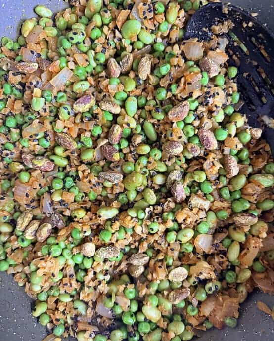 Adding black sesame seeds and pistachios to the peas, edamame, cauliflower saute