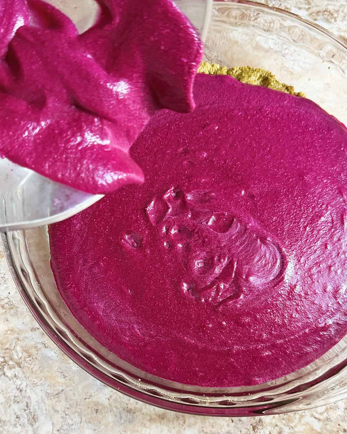 Pouring beet white chocolate filling over pistachio crust
