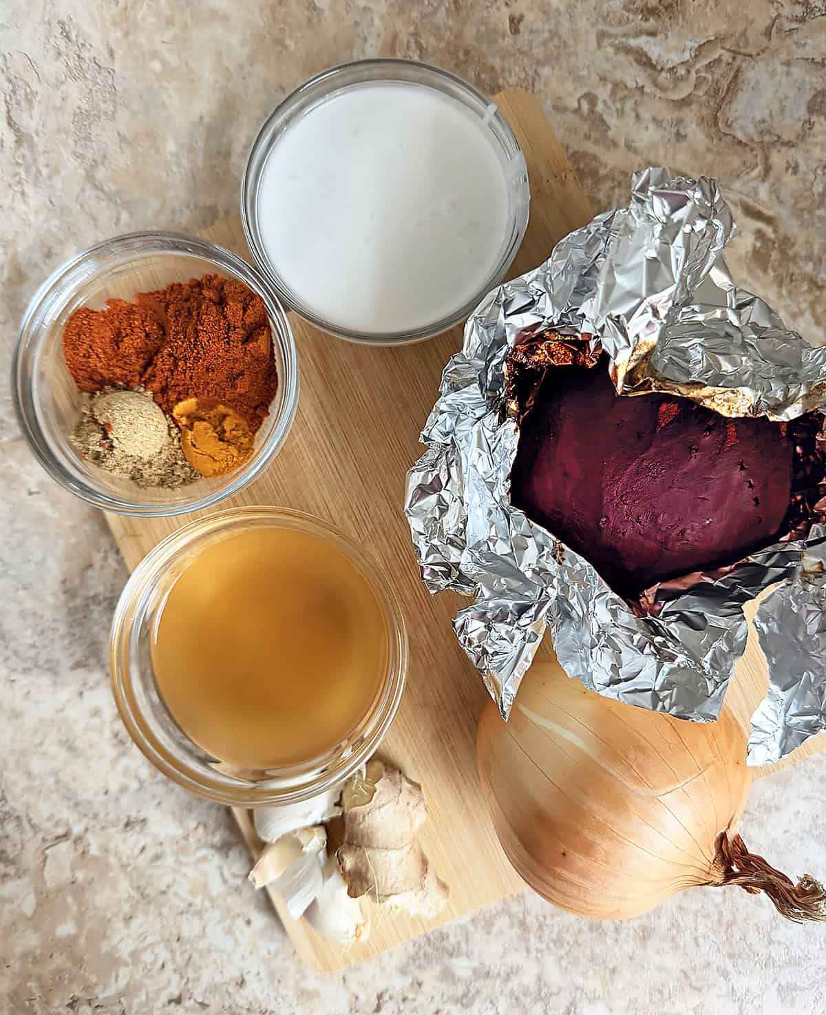 The main ingredients: beet, onion, ginger, garlic, spices, coconut milk, vegetable stock, and cilantro laid on a wooden board.