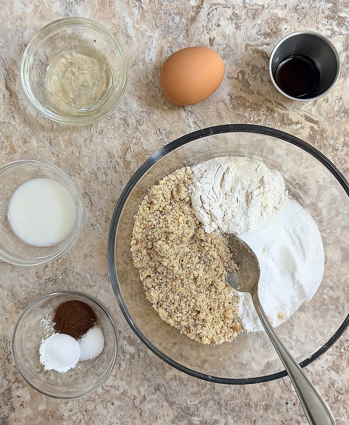 Assorted baking ingredients including flour, egg, vanilla, and spices on a kitchen counter.