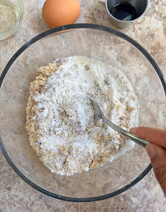 Mixing dry ingredients for baking in a glass bowl with a spoon.
