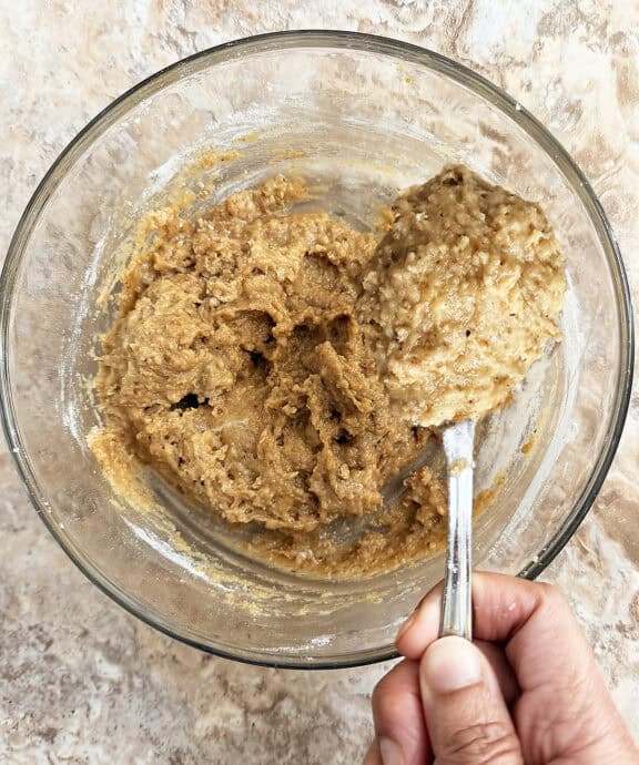 Cookie dough in glass bowl with spoon, ready for baking or chilling.